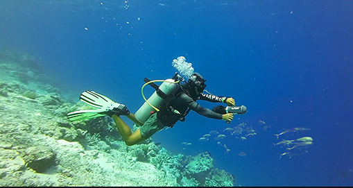 A scuba diver using an underwater scooter above a sunlit reef